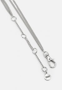 Silver chain accessory with links, featuring a lobster clasp and circular tag. Text reads "DKNY." Smooth, metallic texture.