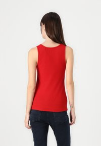 Débardeur rouge côtelé avec un col rond et un design sans manches, associé à un jean bleu foncé. Texture lisse et silhouette ajustée.