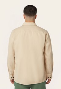 Beige overhemd met lange mouwen, textuurstof, puntige kraag en knopen op de mouwen. Eenvoudig en getailleerd ontwerp, gezien vanuit de achterkant.