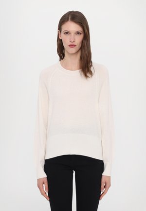 Maglione beige chiaro realizzato in tessuto morbido e leggero. Presenta un collo a giro, maniche lunghe e un orlo posteriore leggermente più lungo.