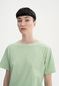 Grünes Kurzarm-T-Shirt aus weichem Stoff, mit Rundhalsausschnitt und einer leicht lockeren Passform. Glatte Textur und minimalistisches Design.