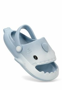 Chanclas en forma de tiburón de color azul claro con bordes redondeados, cuerpo texturizado y diseño de boca abierta. Presenta una correa en la parte posterior y detalles de ojos negros.
