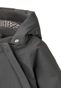 Harmaa vedenkestävä takki, jossa on turkiksella reunustettu huppu, ruudullinenvuori, metallinen painonappisuljin ja resorit hihansuuissa.