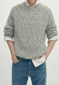 Pull en tricot gris avec un motif texturé, col rond et manches retroussées. Associé à un jean en denim bleu clair.