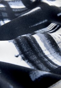 Gros plan sur un tissu texturé avec des motifs abstraits de coups de pinceau noirs, blancs et gris créant un effet dynamique en couches.