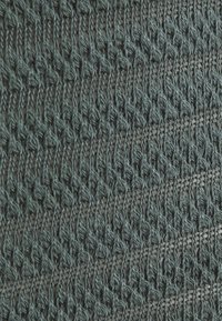 Knit fabric in dark teal, featuring a textured pattern of interlocking stitches, with a soft, textured finish and delicate, open weaves.