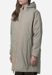 Veste imperméable gris clair avec une fermeture éclair, dotée d'une fermeture éclair multicolore rayée, d'une capuche et de poches latérales. Tissu lisse et texturé.