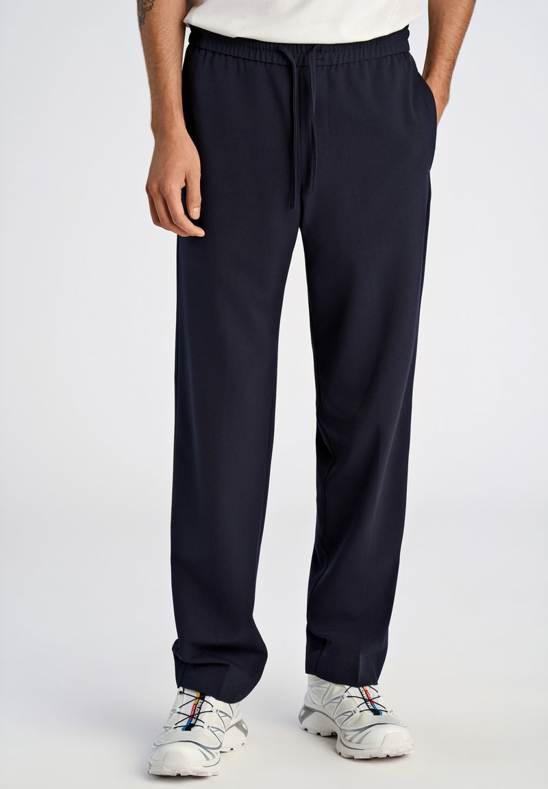 Pantalons de survêtement bleu marine avec une taille élastique et un cordon de serrage, dotés de poches latérales et d'une texture lisse et douce.