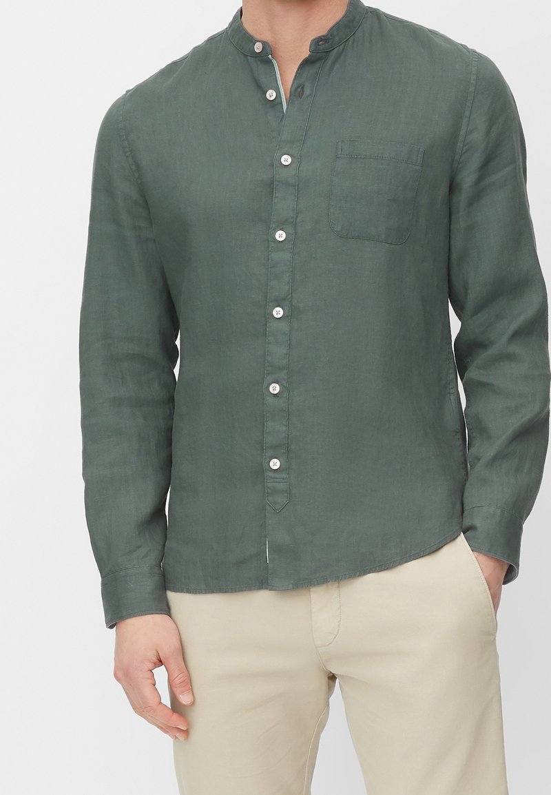 Zielona lniana koszula z długim rękawem, kołnierzykiem typu mandarynka, przednią kieszenią i zapinana na guziki. Tkanina ma fakturowany wygląd.
