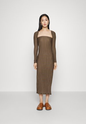 Vestido midi xadrez castanho com mangas longas, decote quadrado, silhueta ajustada e textura suave, combinado com sapatos castanhos de calçar.