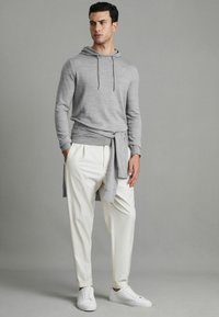 Grauer leichter Hoodie mit einer Kordel, über weißen plissierten Hosen getragen und mit weißen Sneakers kombiniert. Glatte Textur und lässige Passform.