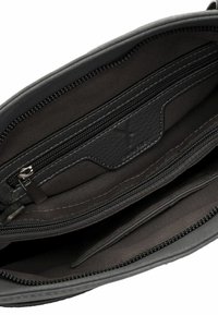 Interior de bolso negro con múltiples compartimentos con cremallera y detalle de cuero cosido.