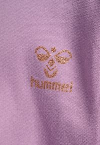 Ljuslila texturerat tyg med en guldfärgad glittrande logotypdesign som inkluderar stiliserade bin och lövelement, samt ordet "hummel" nedanför.
