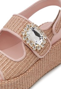 Light pink synthetic wedge sandal with woven texture and large jewel embellishment. Features open toe and ankle strap for secure fit.