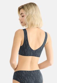 Tamsiai pilkas sportinis liemenėlė su žemu nugaros dizainu, plačiomis petnešomis ir tekstūruota vertikalių baltų linijų raštu. Minkšta, tampri medžiaga.