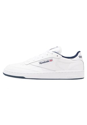 Baskets Reebok blanches à coupe basse avec doublure marine, logo Reebok, écusson du drapeau Union Jack et semelle texturée sur fond blanc.