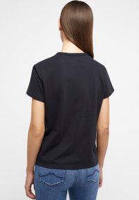 T-shirt in cotone nero con maniche corte, scollatura rotonda e una texture liscia. Abbinato a jeans in denim con design della tasca posteriore.