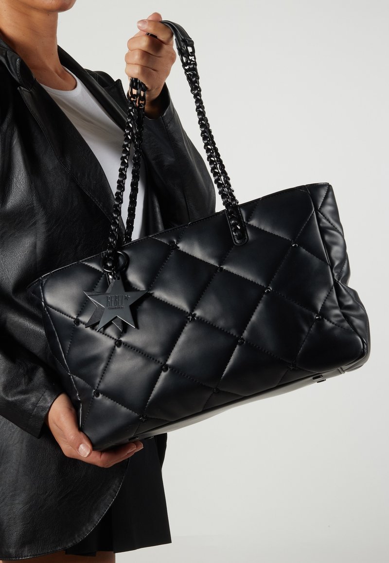 Mustat tilkkukassit, jotka on valmistettu synteettisestä materiaalista, sisältävät ketjuolkaimia ja tähdenmuotoisen etiketin, jossa on teksti "REBEL."