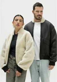 Lysebeige shearling bomberjakke med sorte rib-strikmanchetter, parret med en sort læderbomberjakke med pelskrave og sidelomme.
