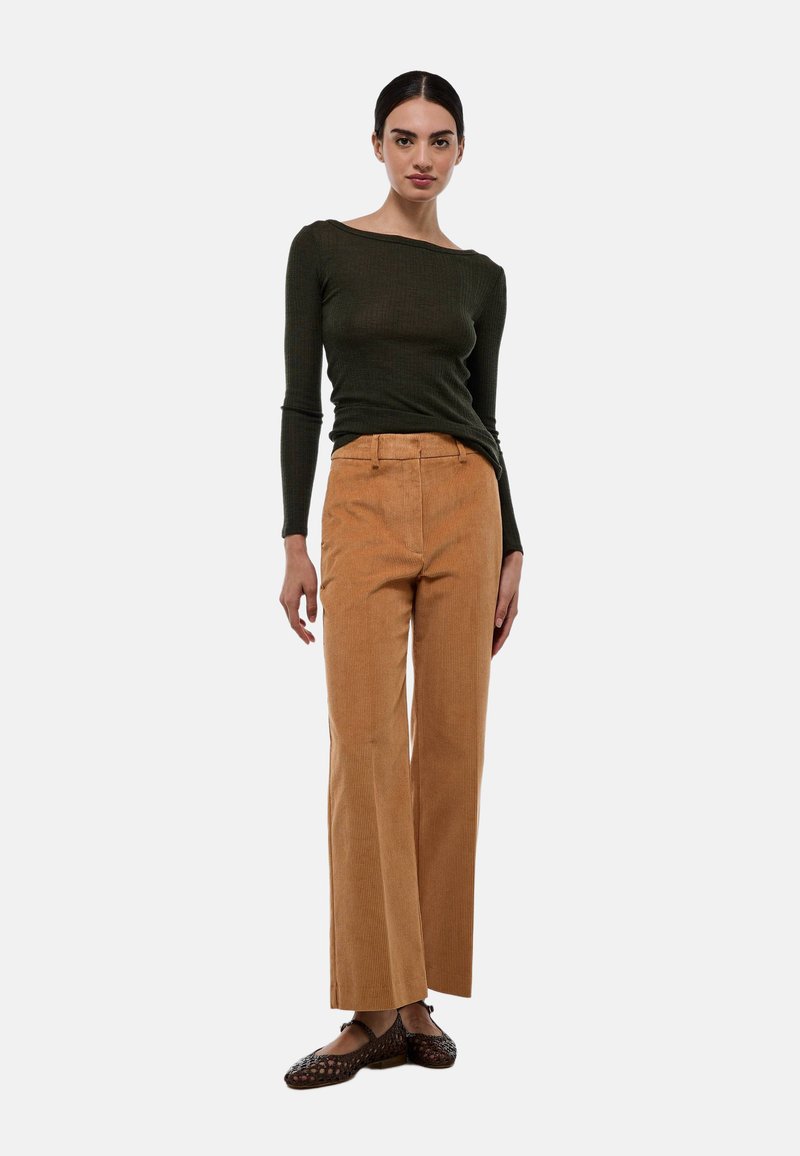 Un haut à manches longues côtelé vert foncé associé à un pantalon large en velours côtelé beige. Des chaussures tissées marron complètent la tenue.