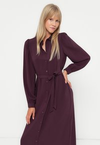 Rochie cămașă din burgundy cu mânecă lungă, cu deschidere cu butoane în față, talie legată și detalii pliate la umeri. Material neted cu o croială lejeră.