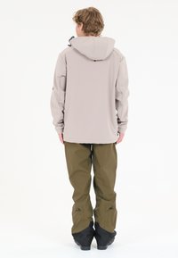 Lys beige softshell jakke med hætte, parret med olivengrønne vandtætte bukser med sorte accenter og justerbare manchetter.