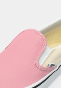 Ροζ πάνινο παπούτσι χωρίς κορδόνια με ραφές και λευκή λαστιχένια σόλα. Στη πλευρά φαίνεται η ετικέτα της μάρκας και το αντίθετο μπεζ εσωτερικό.