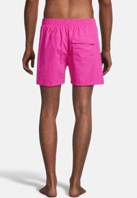 Shorts de bain roses vifs en tissu léger. Dotés d'une taille élastique et d'une poche latérale avec fermeture à bouton.