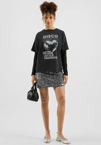 Czarny t-shirt graficzny z napisem "DISCO" oraz nadrukiem dyskotekowej kuli w kształcie serca, nałożony na srebrną spódnicę mini z cekinami. Srebrne buty na kostkę z paskiem i czarna torebka.