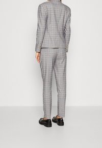 Szary garnitur w kratę z dopasowaną marynarką i obcisłymi spodniami. Na rękawach marynarki złote guziki. Noszony z czarnymi butami.