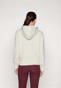 Light beige hoodie with a hood, ribbed cuffs, and hem, paired with burgundy leggings. Soft fabric texture, minimalistic design.