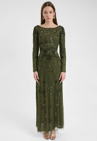 Lungo abito verde oliva con intricati motivi floreali in perline e paillettes, maniche lunghe e silhouette dritta, abbinato a scarpe aperte.