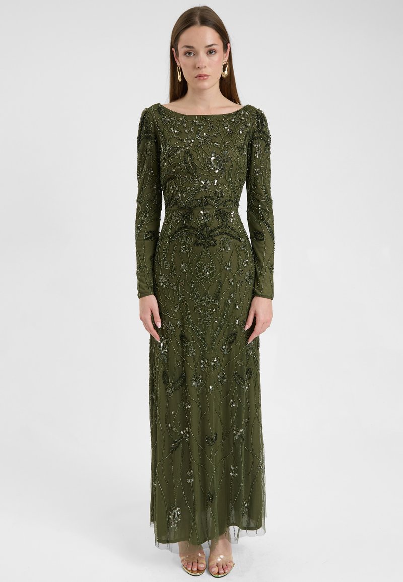 Lungo abito verde oliva con intricati motivi floreali in perline e paillettes, maniche lunghe e silhouette dritta, abbinato a scarpe aperte.
