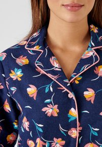 Navyblauwe pyjama top met een bloemenpatroon in roze, geel en turquoise. Heeft een notch-kraag, roze piping en knopen aan de voorkant.