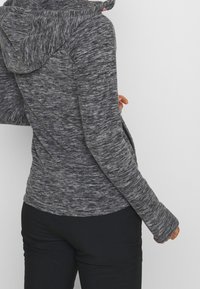 Gray athletic hoodie with a textured finish, long sleeves, and a fitted design. Features a hood and a curved hem. Paired with black pants.