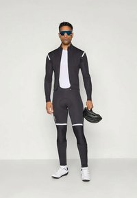 Juodas dviratininko kostiumas, sudarytas iš prigludusios striukės ir tamprių su baltais dryžiais. Modelis laiko juodą šalmo ir vilki sportinius akinius.