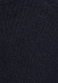 Gros plan d'un tissu tricoté bleu marine foncé avec un motif texturé et des fibres douces visibles.