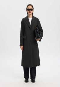 Lång mörkgrå kostymrock med skräddarsydd passform, enkel knappstängning, skörlappar och sidofickor. Bärs över en vit topp.