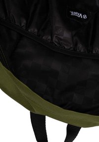 Interior de mochila de tela verde con un patrón a cuadros negros y una etiqueta de logo de Vans. Presenta una textura suave y forrada.
