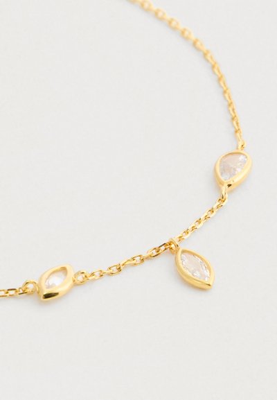 Λεπτή χρυσή αλυσίδα με τρία μικρά διάφανα πετράδια σε σχήματα σταγόνας και μαρκίζ, σε φωτεινό φόντο.