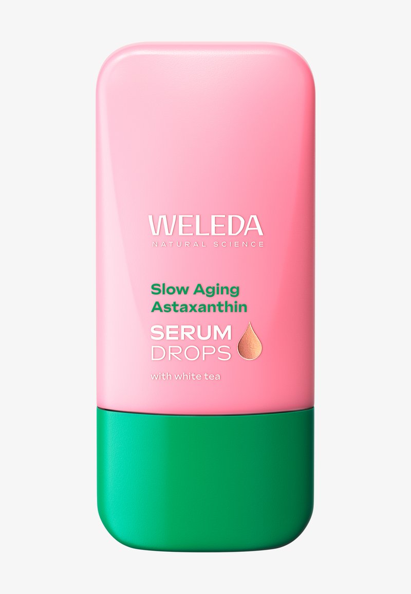 Bottiglia di gocce Weleda Slow Aging Astaxanthin Serum di colore rosa e verde con tè bianco, mostrata su sfondo bianco.