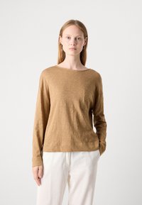 Langermet, brun topp laget av myk stoff med rund hals og en liten lomme på brystet; kombinert med hvite, strukturerte bukser.