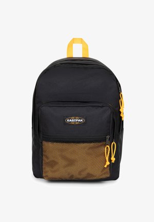 Czarny plecak z żółtym górnym uchwytem i akcentami, z siatkową przednią kieszenią i zamkami błyskawicznymi. Wyraźnie widoczne logo Eastpak.