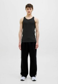 Czarny ribbed top bez rękawów w połączeniu z luźnymi czarnymi spodniami z białymi bocznymi paskami. Model stoi na tle jednolitej białej ściany.