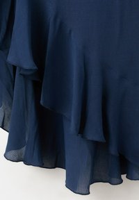 Čeveljasto temno modro blago z večplastnimi robovi z volančki in polprosojno teksturo, ki visi v mehkih, ukrivljenih gubah.