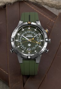 Hodinky Timex Expedition s zeleným gumovým remienkom, nerezovým puzdrom, čierno-žltými akcentmi a multifunkčným ciferníkom s údajmi o prílivoch a kompasom.