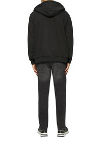 Schwarzer Baumwoll-Hoodie mit Kapuze, gerippten Bündchen und Saum. Kombiniert mit dunkelgrauen Jeans und schwarz-weißen Sneakers.