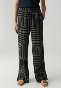 Losse, gemusterde broek in donker groen en marineblauw met geometrische lijnen. Voorzien van een elastische tailleband en zijzakken. Glad stof.