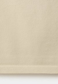 Gros plan d'un tissu tricoté beige montrant une texture tissée et un ourlet plié au bord inférieur.