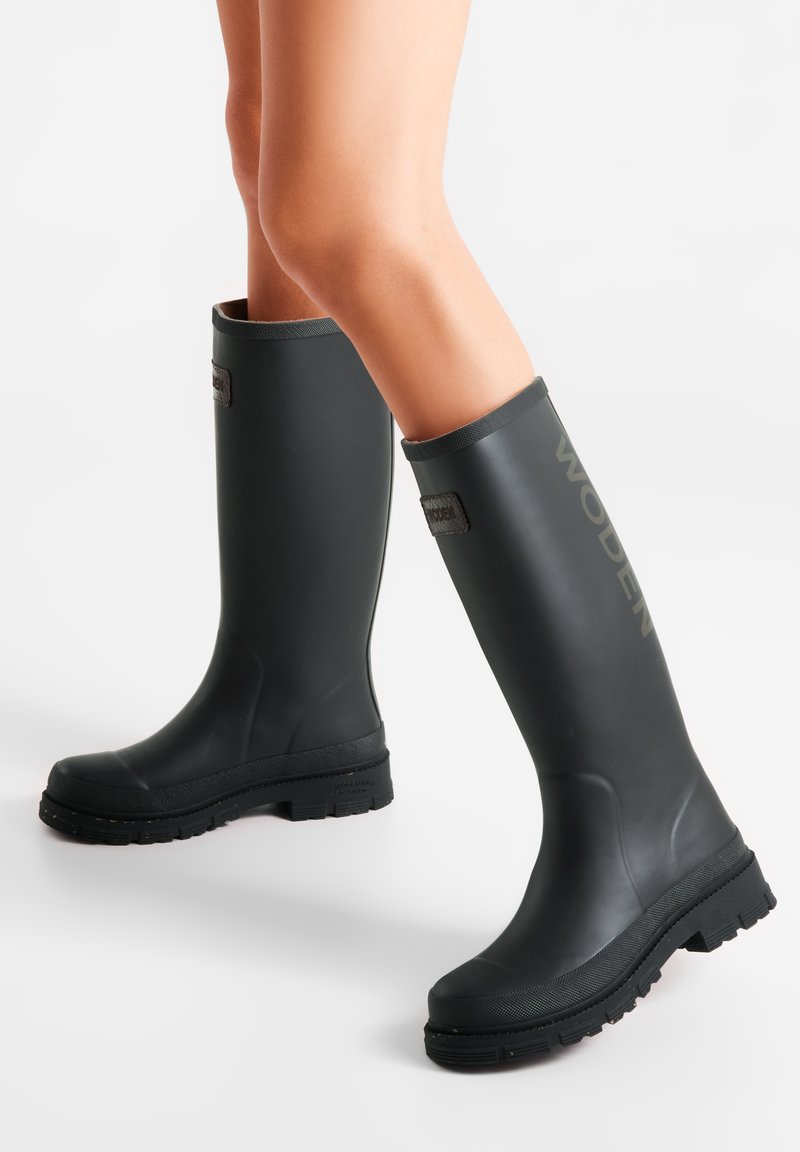 Bottes de pluie en caoutchouc noir avec une semelle texturée, un haut tige et une étiquette logo sur le côté ; conçues pour une protection imperméable.